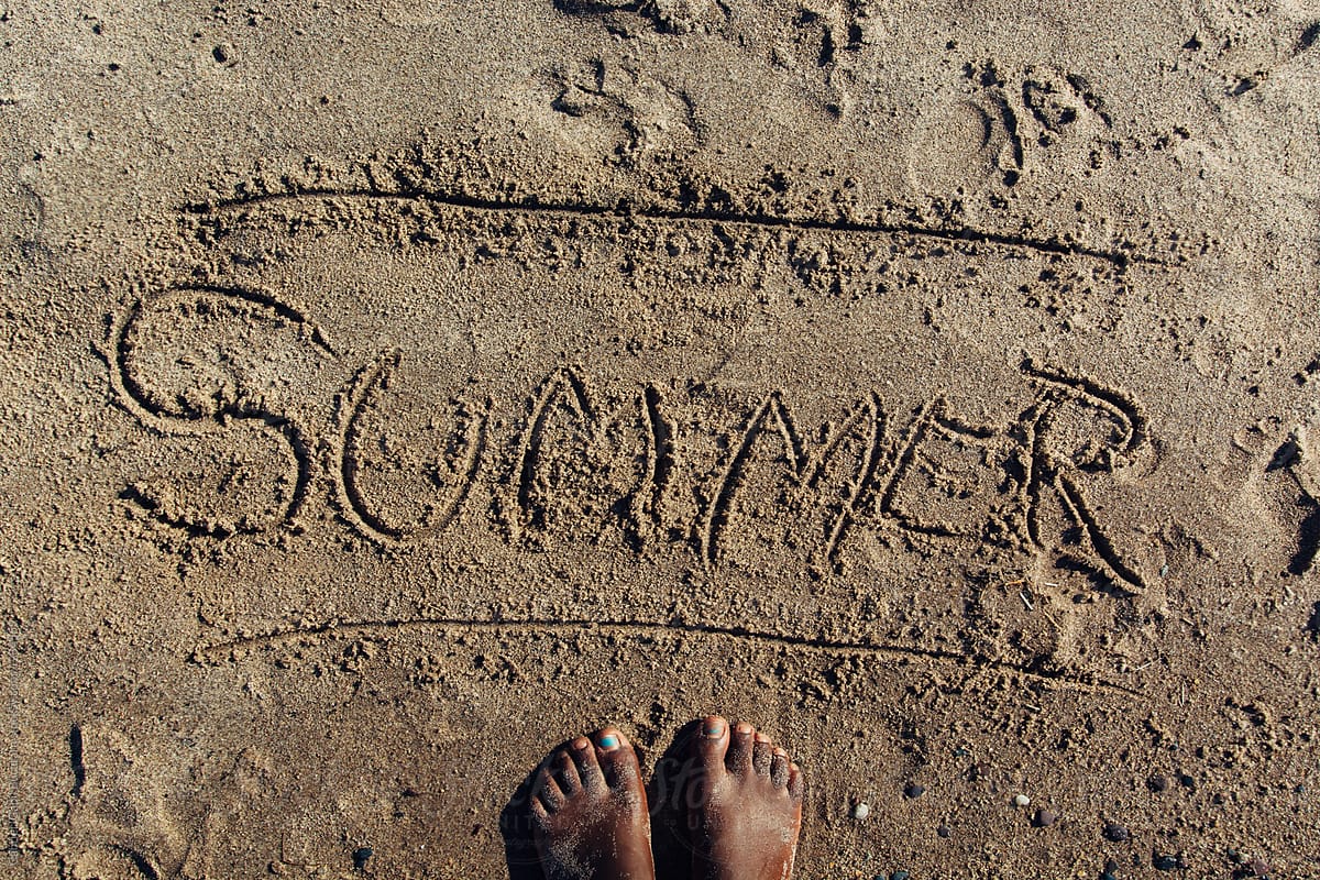 Black girl\'s feet next to scribbled summer in the sand