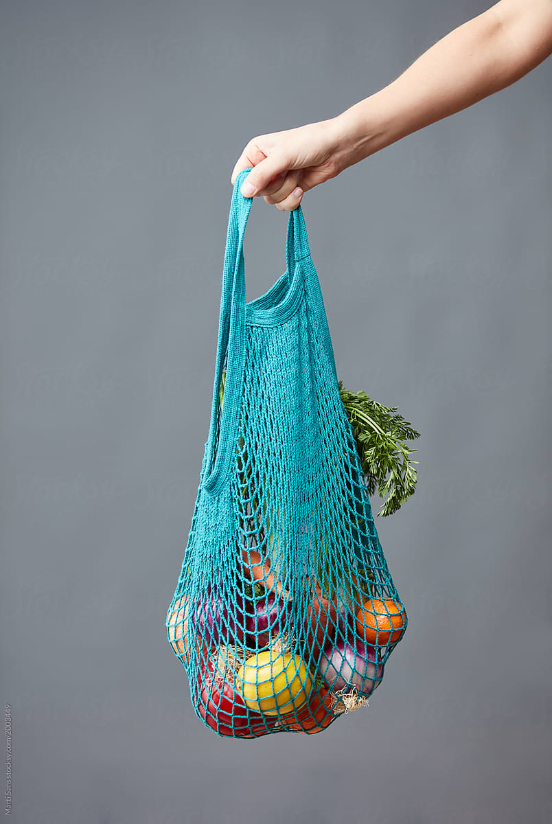 Hand holding blue reusable bag full of vegetables.