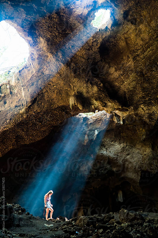 A young woman standing in a beam of light in a cave in Indonesia