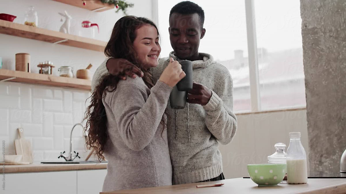 Interracial Couple Drinking And Hugging In Kitchen By Stocksy