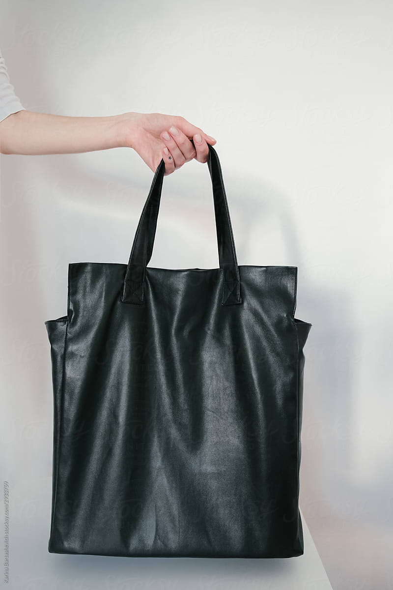 photo of a large classic black bag held by a man’s hand against a white wall
