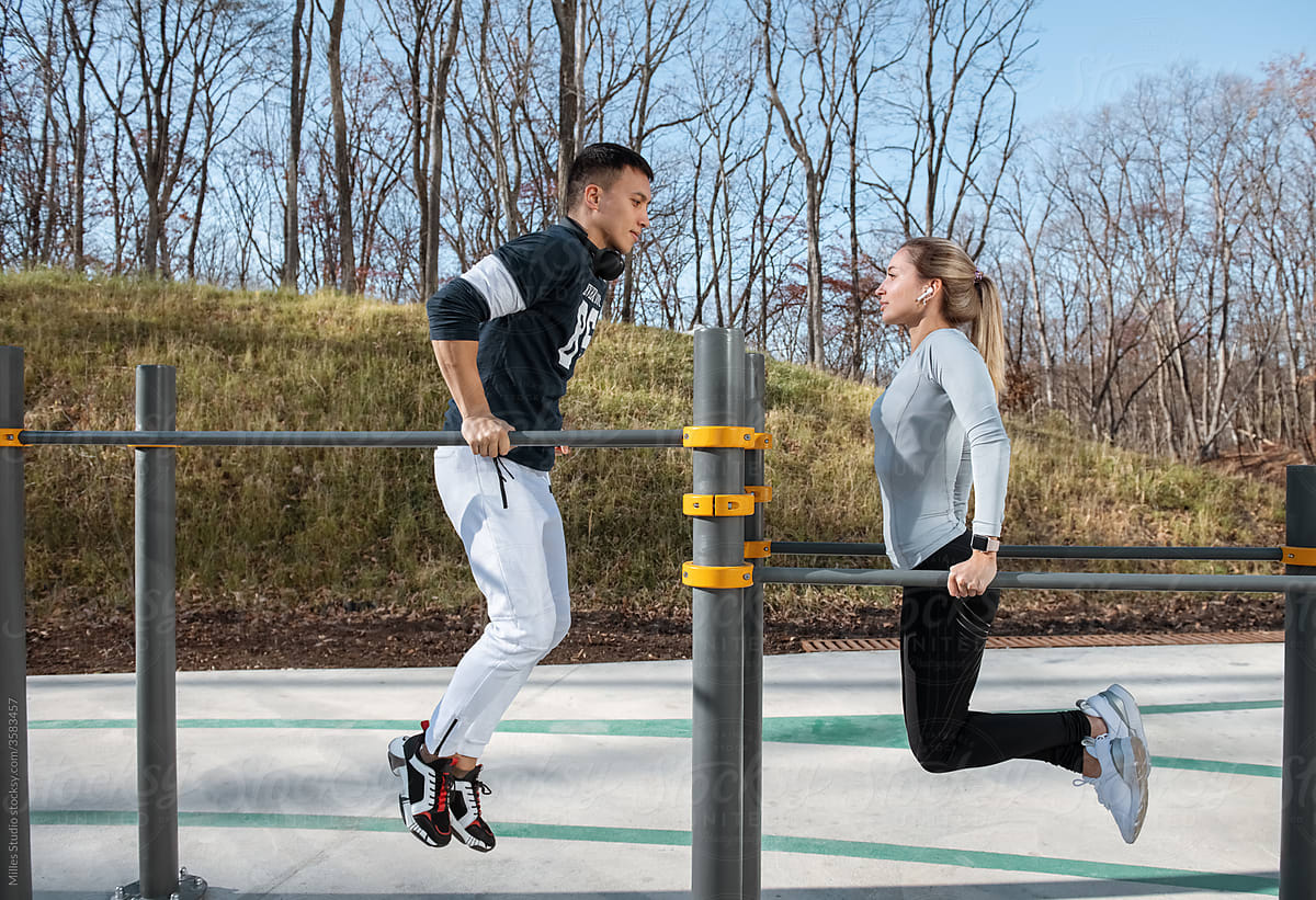 Sportsman and sportswoman exercising on bars in park