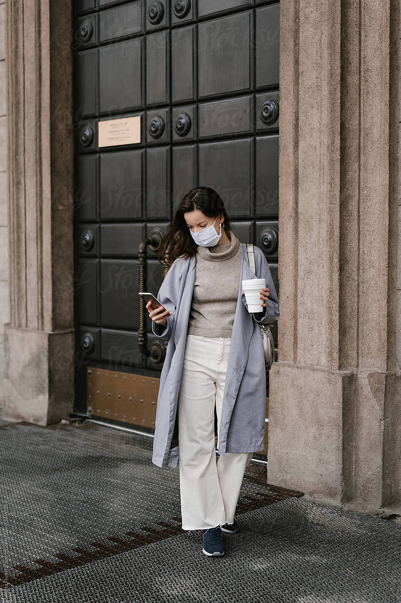 Stylish woman in mask using smartphone on street
