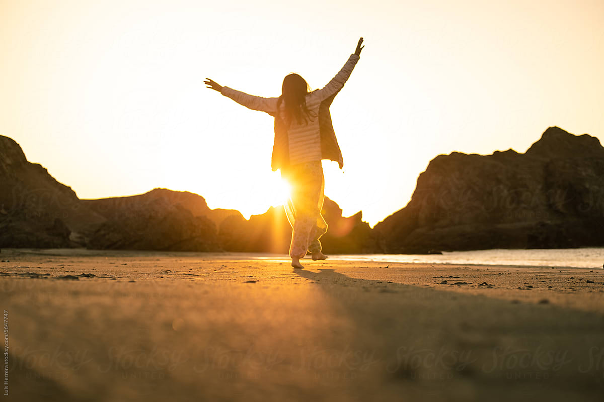 carefree woman walking on the beach at sunset with arms up