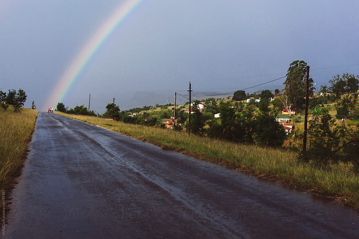 Three figures walk into light of double rainbow on road