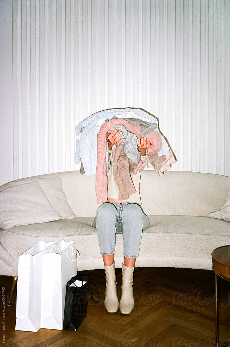 Anonymous female covering face with pile of clothes in arms