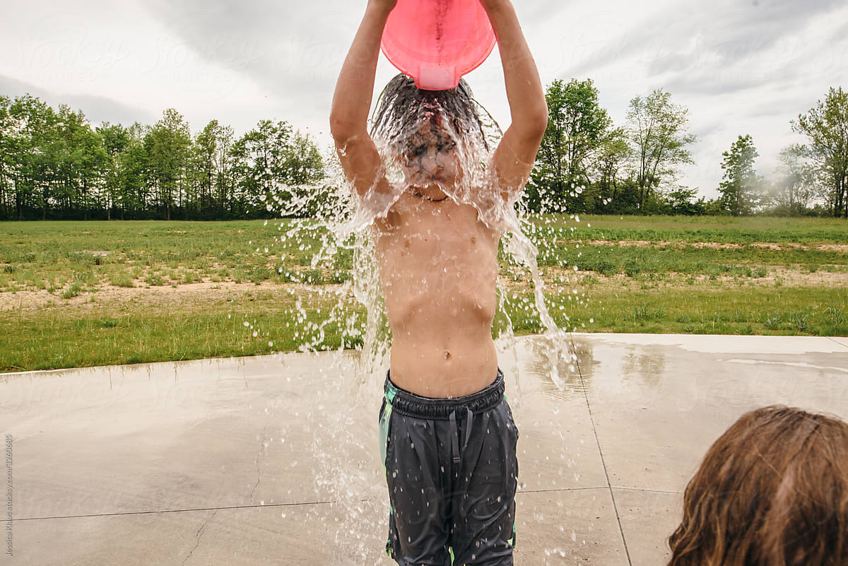 Boy dumping bucket of water over head.