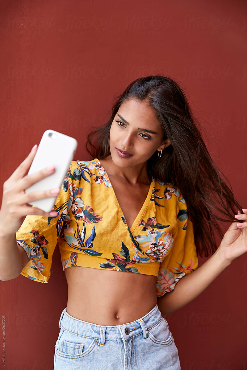 Woman with smartphone smiling and taking selfie straightening hair