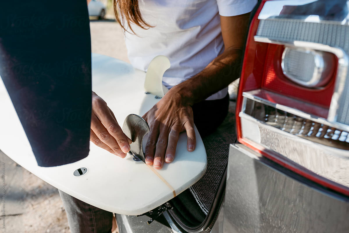 Long hair man waxing surfboard on car