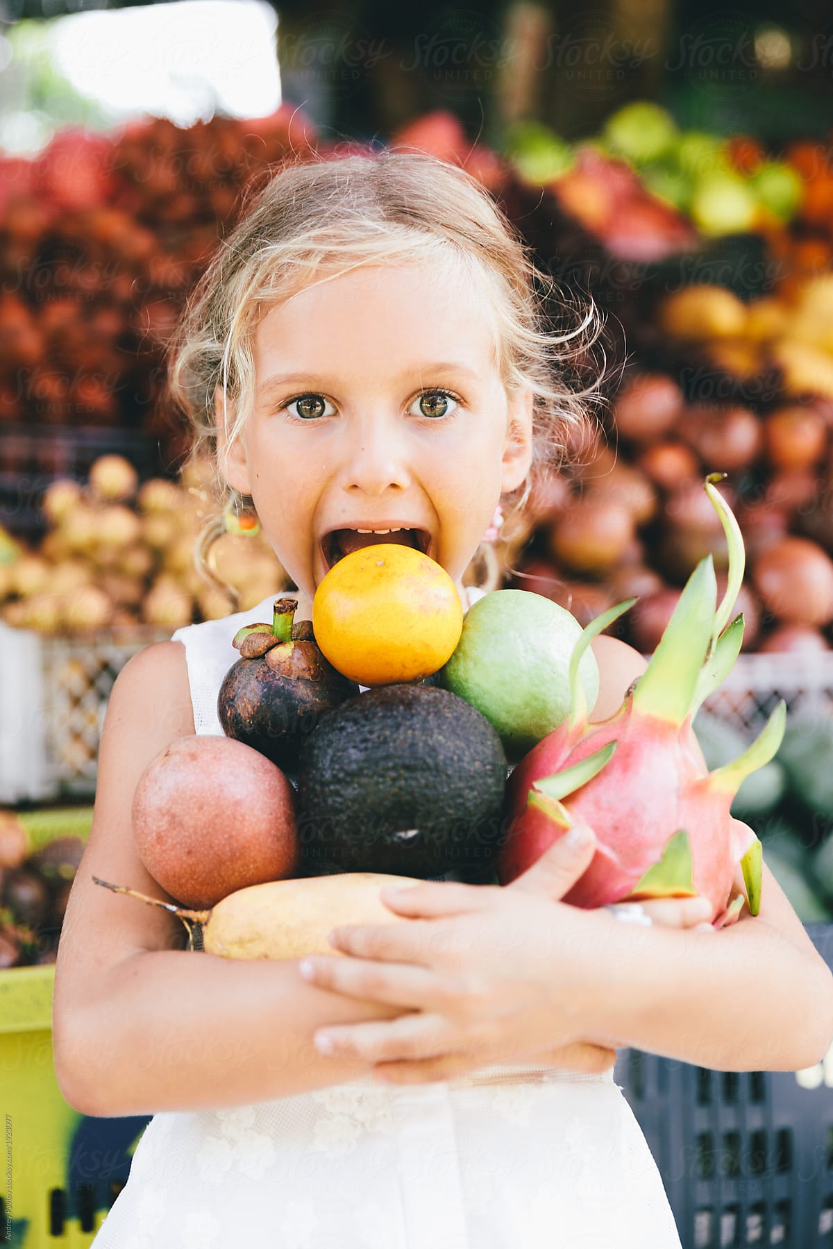 The child holding a bunch of fruits in the fruit store