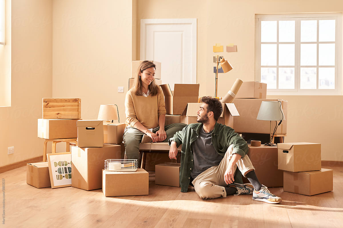 Glad man and woman resting near belongings in new flat