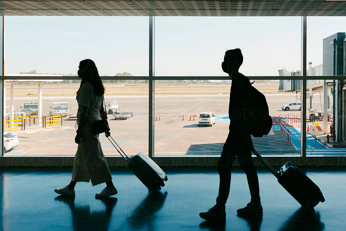 Silhouette of travelers with carry-on luggage on airport terminal