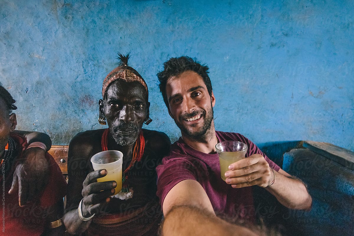 Selfie of an African Hamer tribe senior man with young traveler having a drink on a local bar. Omo valley, Ethiopia