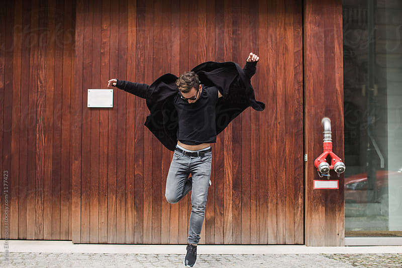 Mann jumping in front of the dark brown wooden wall