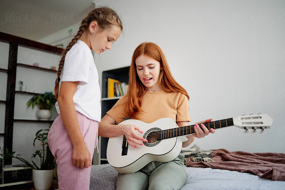 Tutor teaching female pupil playing on guitar indoor
