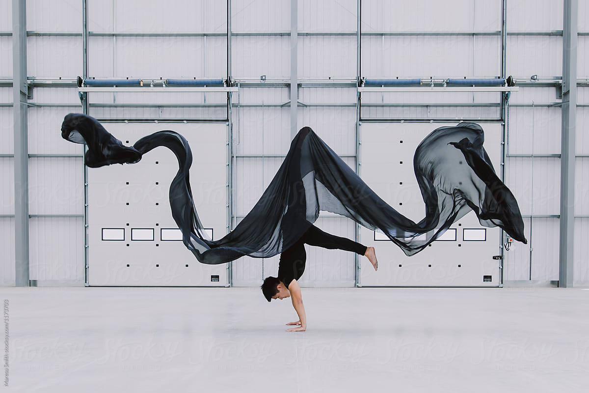 A dancer lifts himself up into a headstand as black silk ripples above him