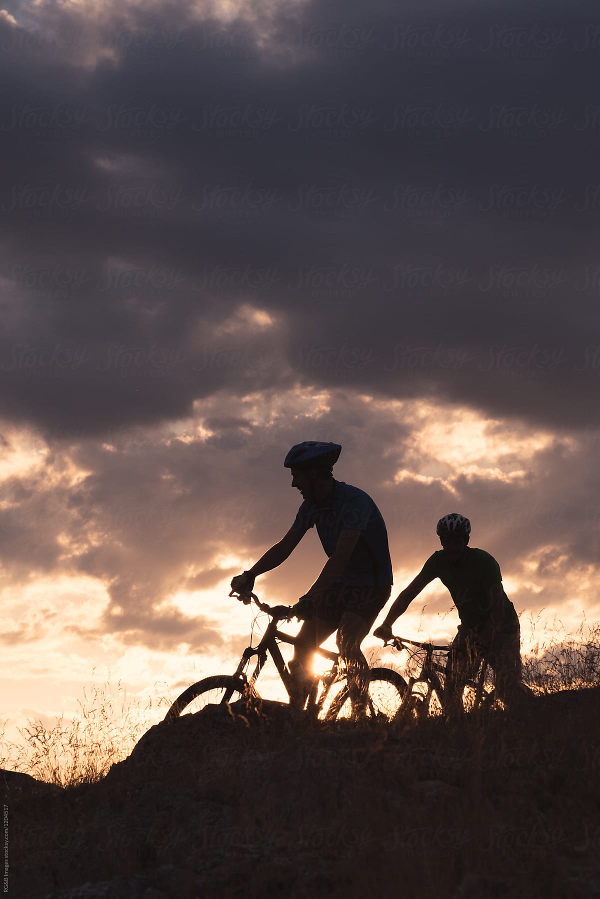 Sportsmen silhouettes riding mountain bikes with sunset sky in backround