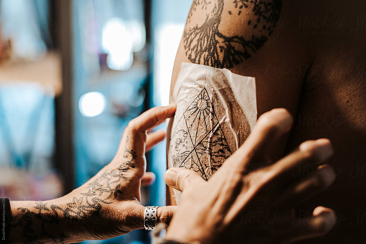 Crop tattooist applying sketch on client arm