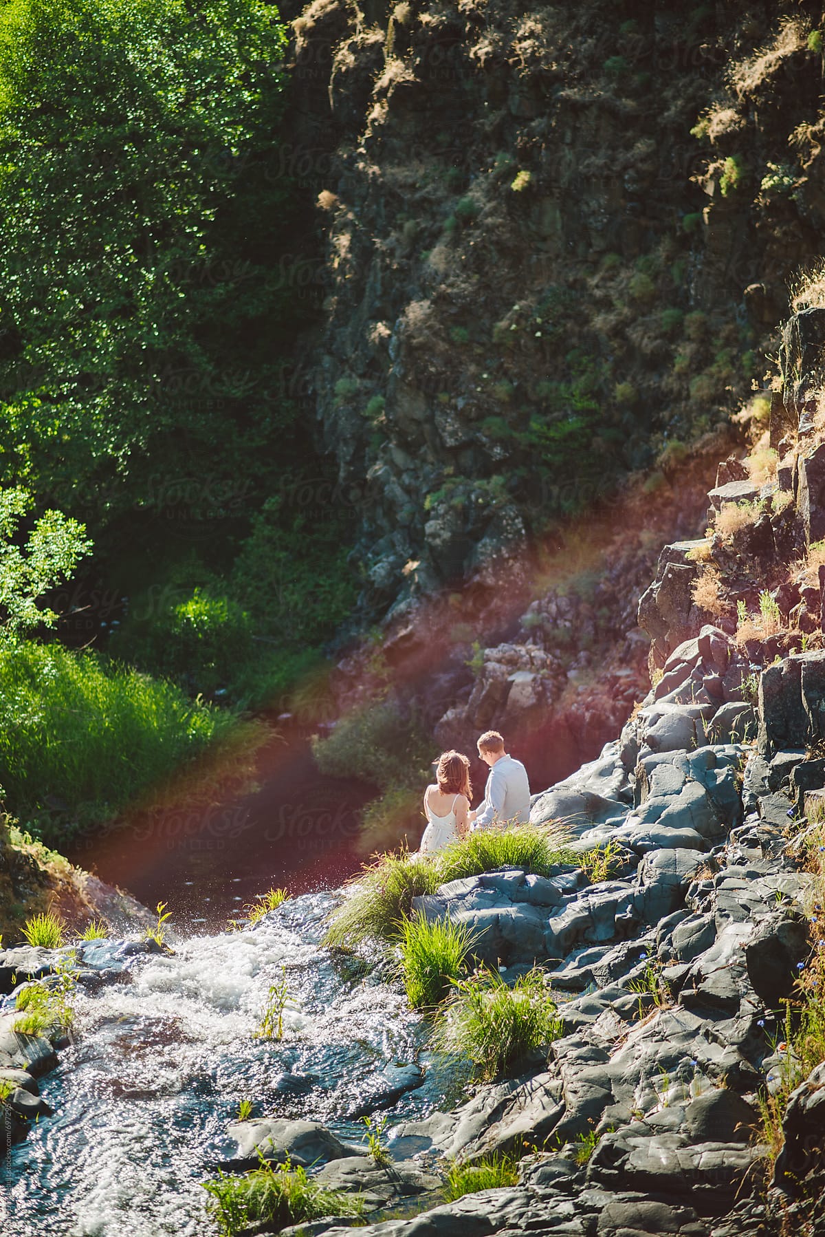 Young couple sitting on a cliff with a waterfall and a rainbow.