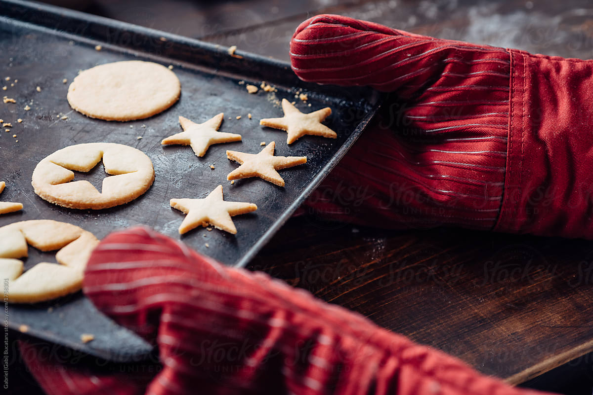 Red oven mittens holding tray with star shaped cookies