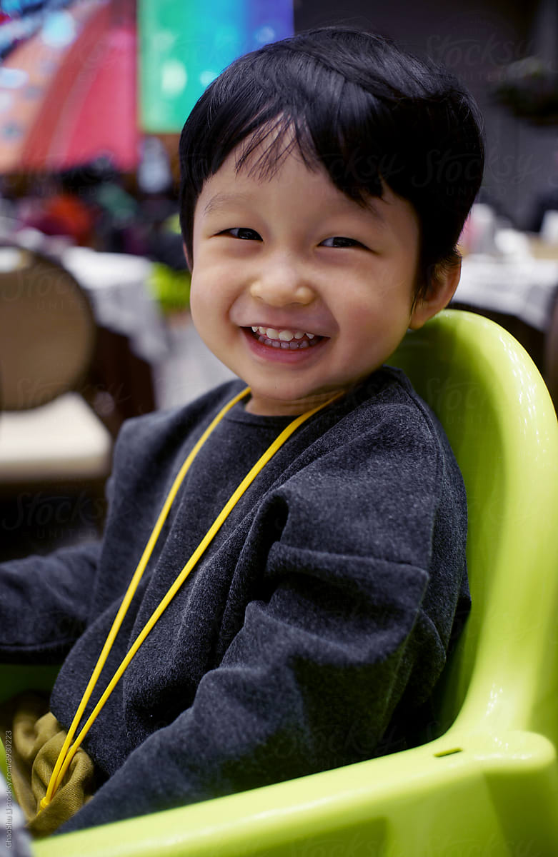 Cute Asian Chinese little boy sitting on a dining chair and playing