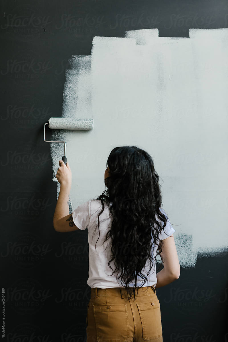 young woman painting new light color over a black wall