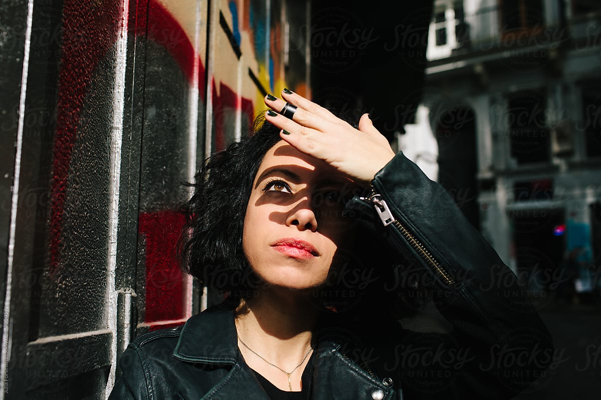 Beautiful woman shields her eyes from the sun on urban street.