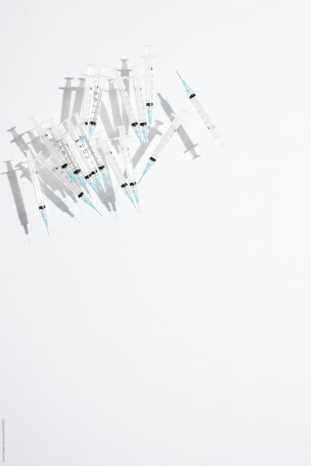 A pile of hypodermic needles casting a shadow in a white surface.