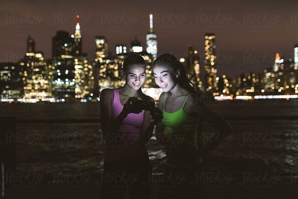Young friends using technology at night against New York skyline