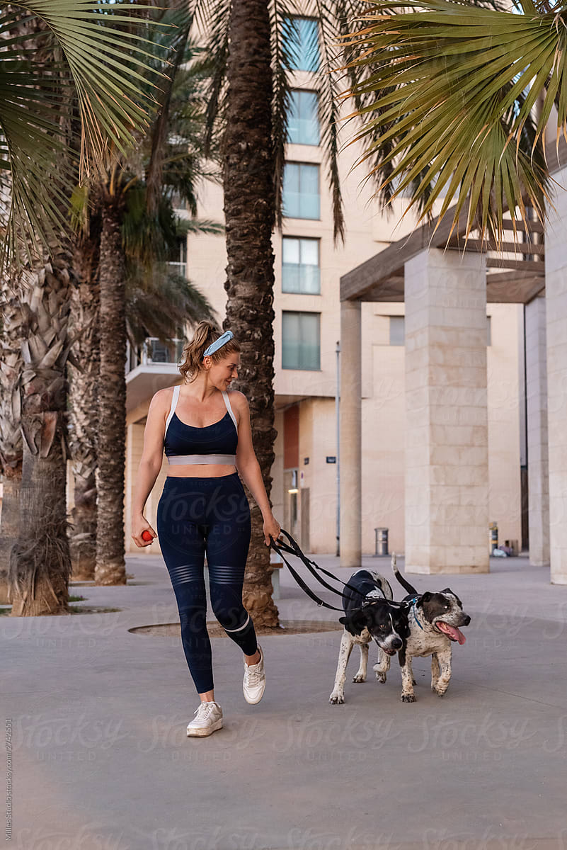 Woman in sportswear walking with dogs on street