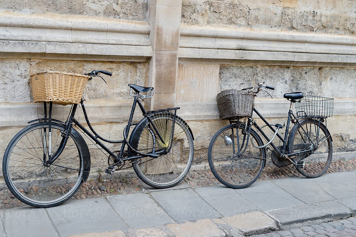 A pair of bicycles with baskets leaning on a wall