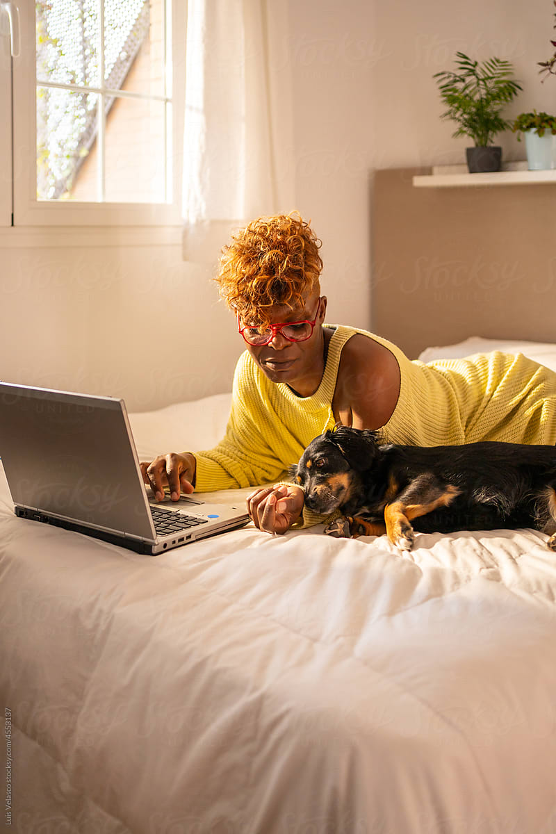 Woman Working From Home On The Bed Next To Her Little Dog.