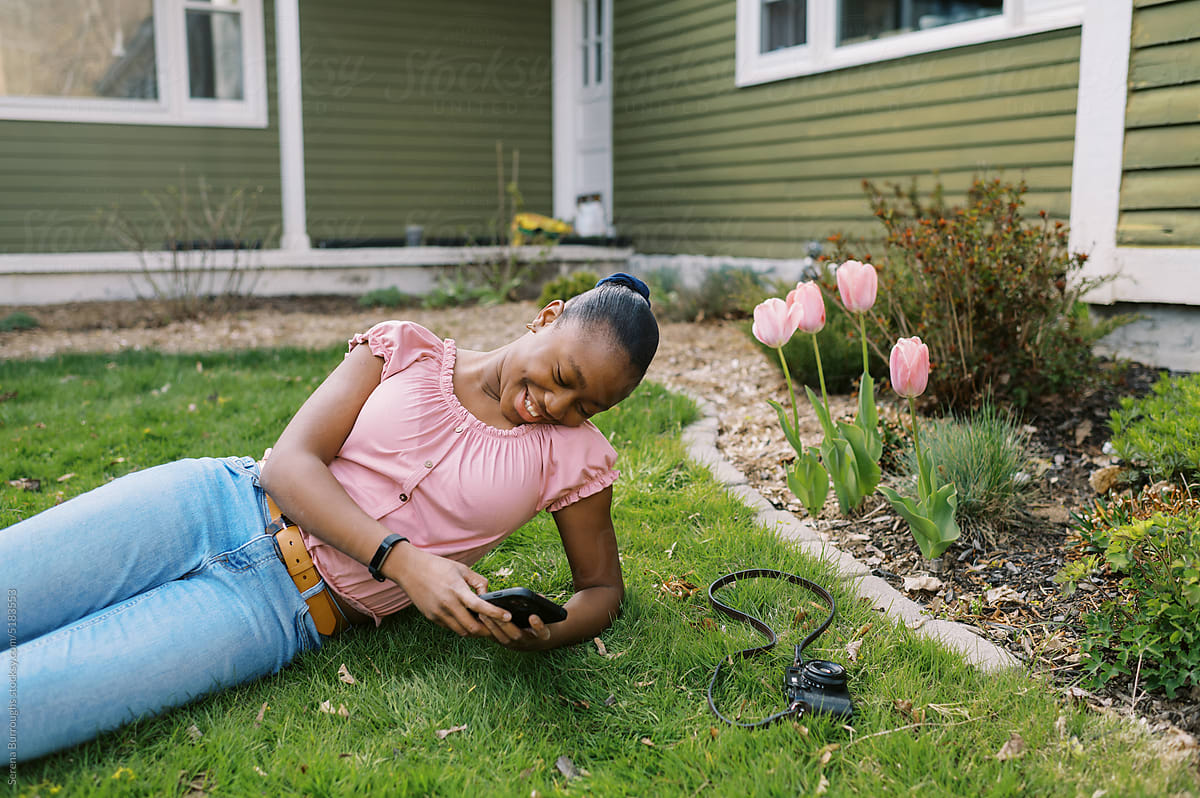 Young black girl sitting outside in yard while using her phone