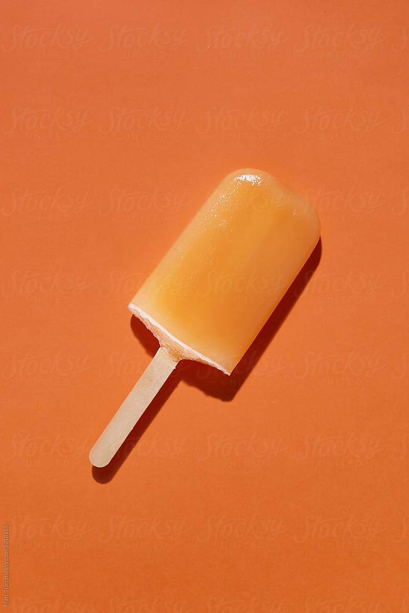 Top view of single orange popsicle on a color background.
