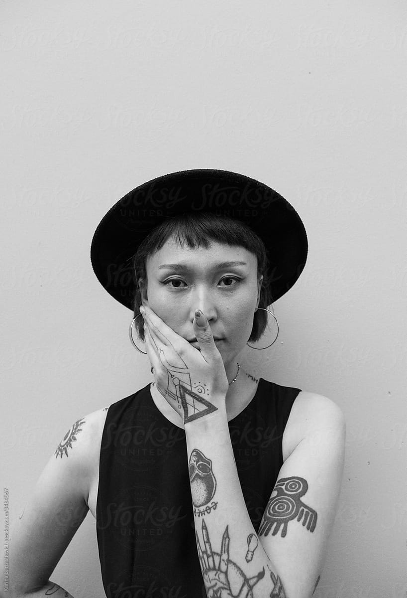 black and white portrait of a stylish girl in a hat, with tattoos on her arms and neck in the parking lot