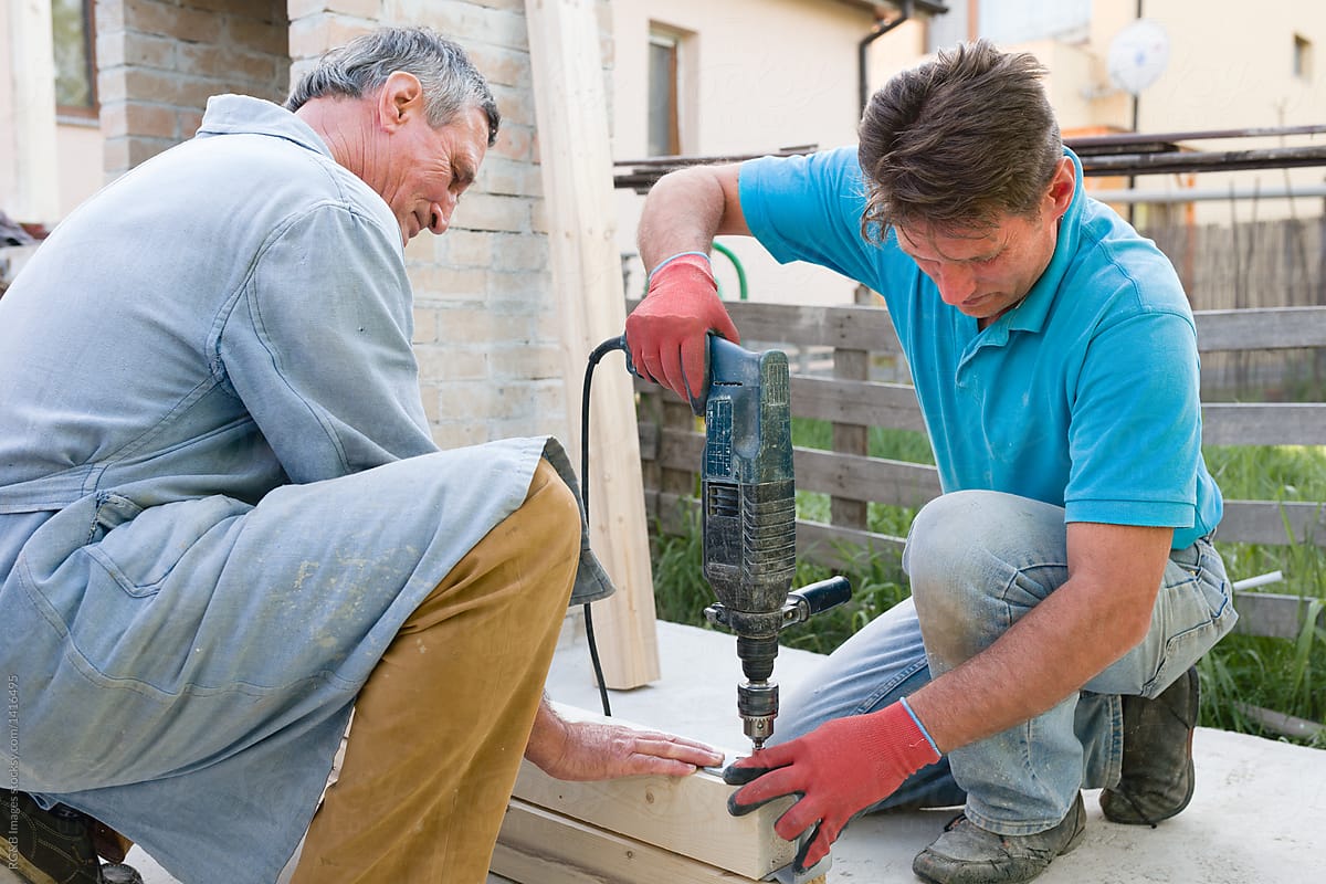 Two men drilling wooden plank for house construction outdoor