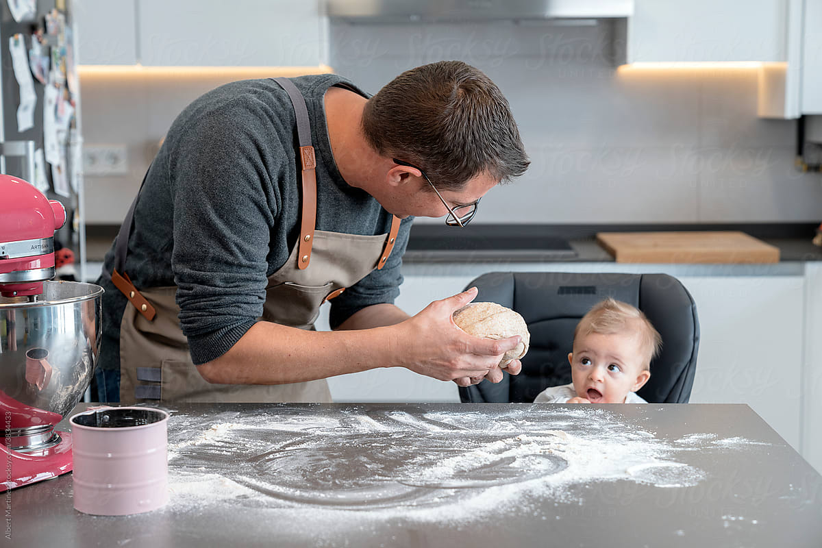 Father showing bread dough to a baby in the kitchen.