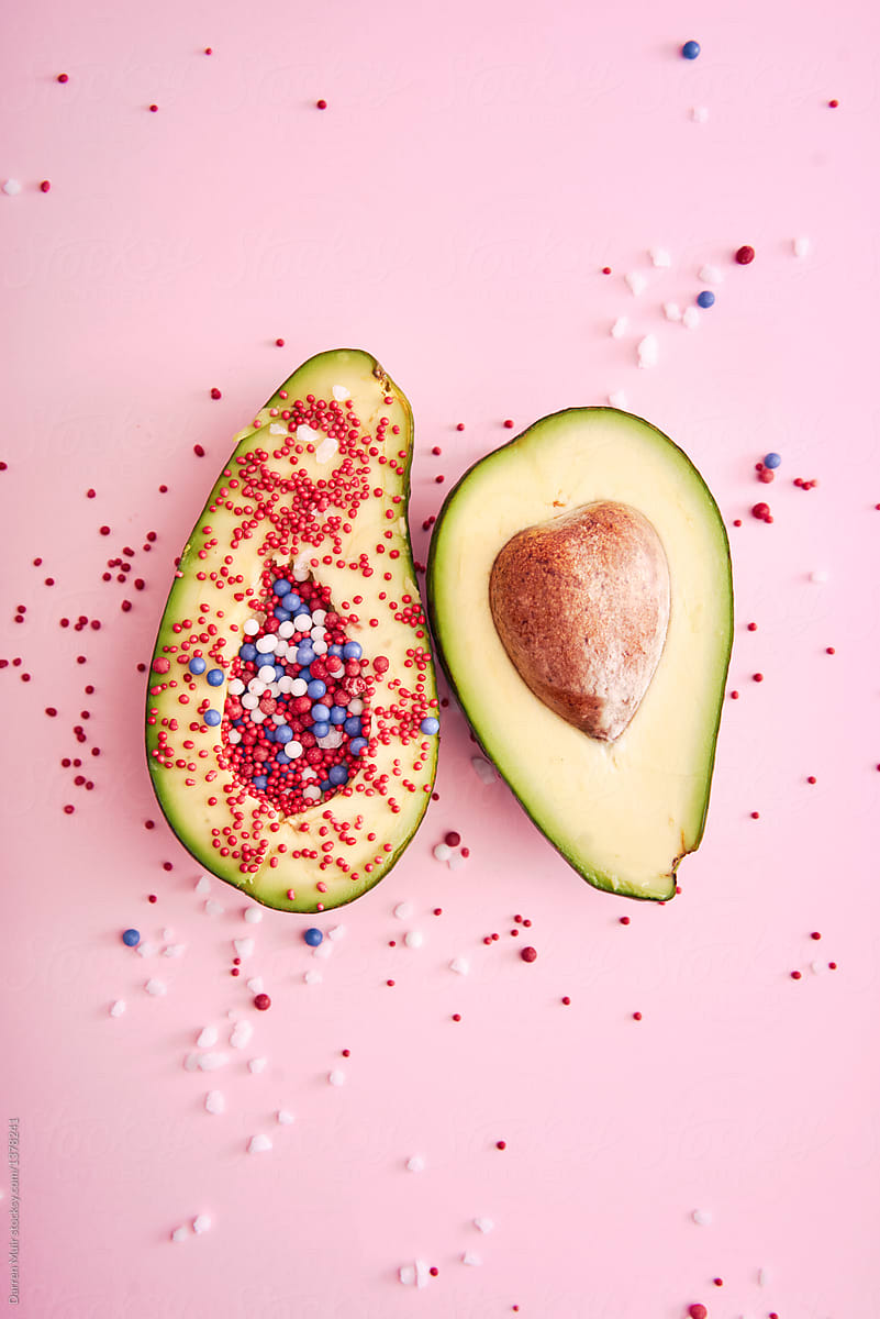 Avocados with candy on pink background.