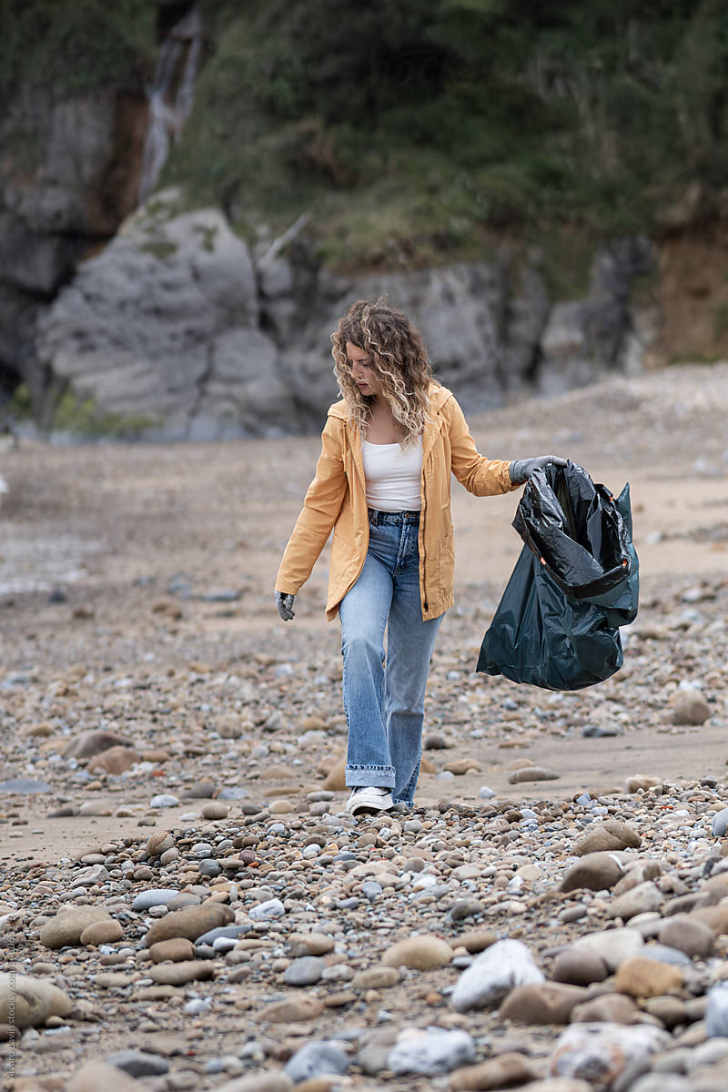 Woman picking up waste from beach.