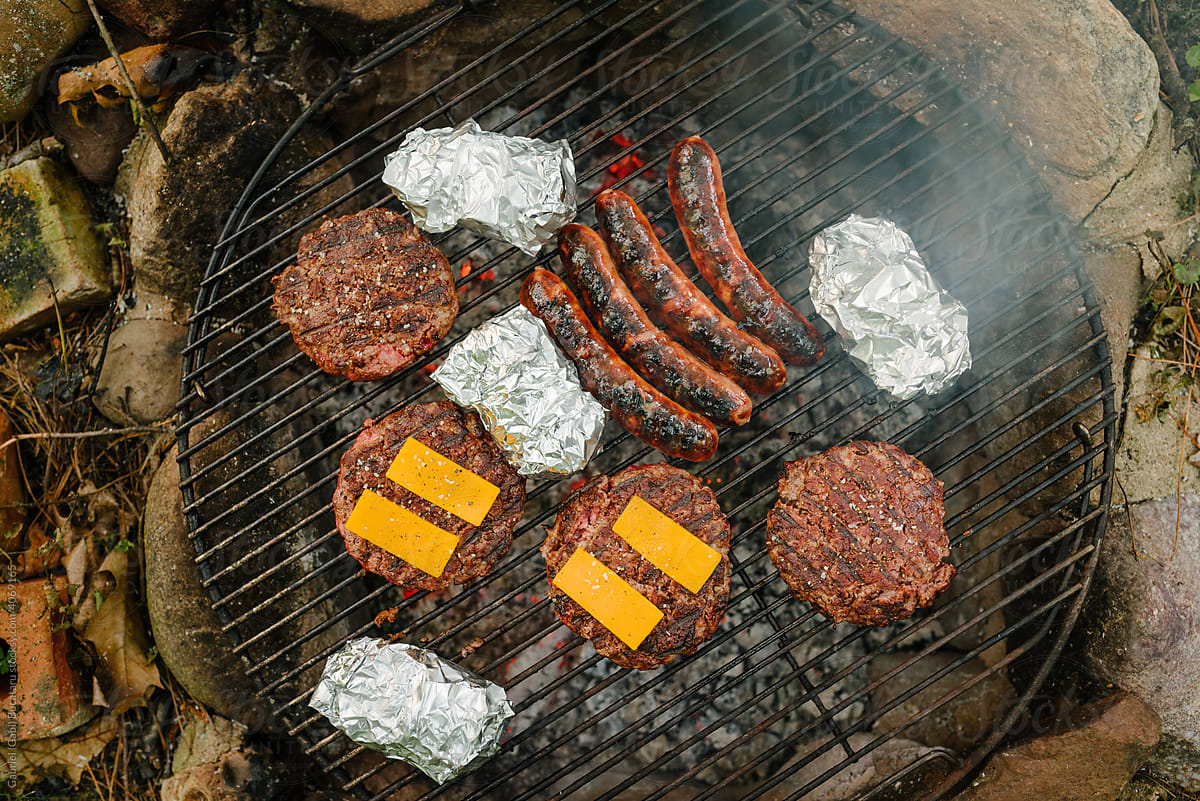 Hamburgers, sausages and baked potatoes on a outdoor grill