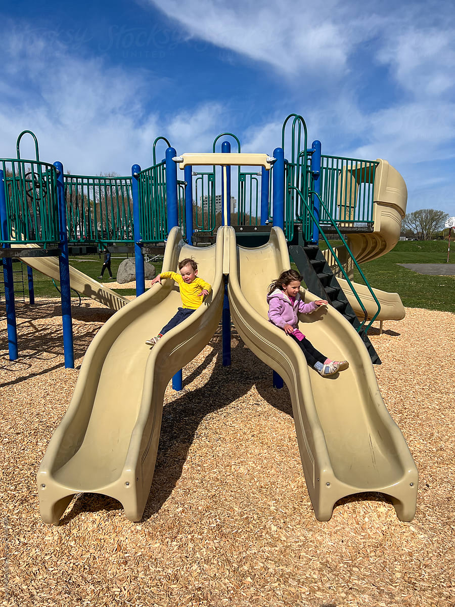 Two Children Play Together on Slide at a Playground