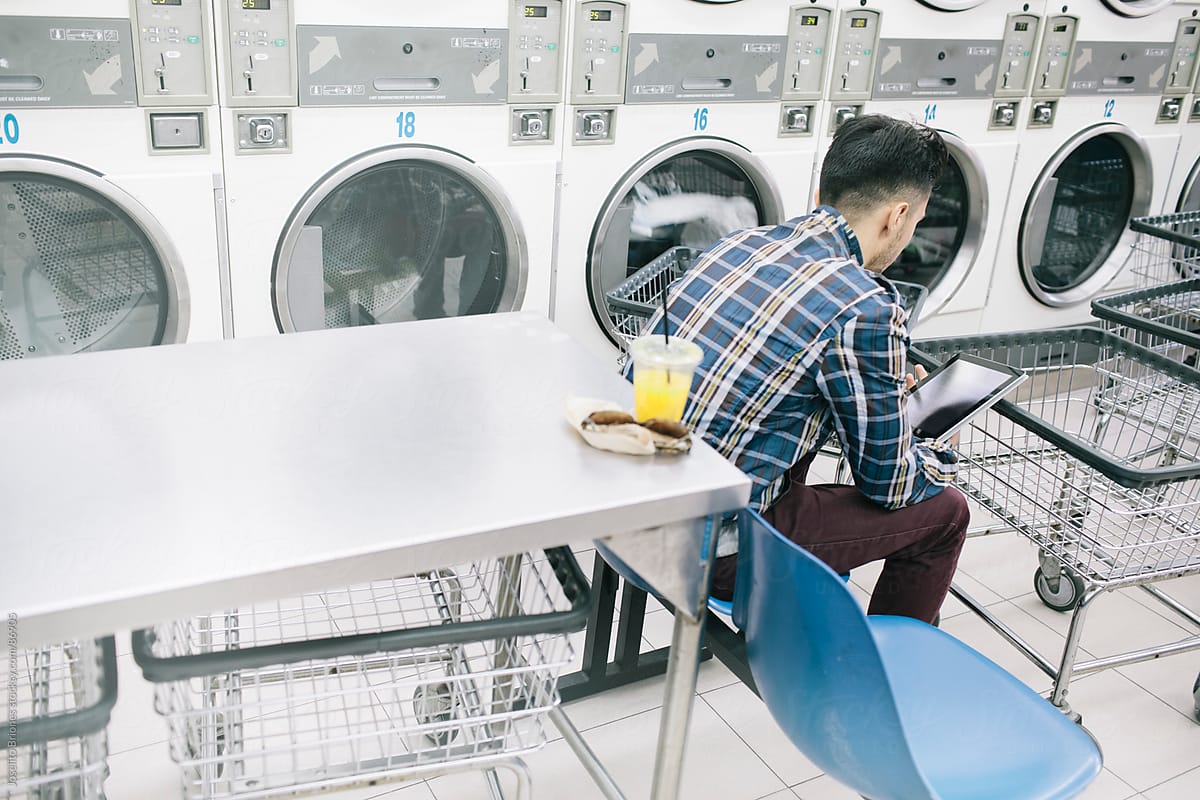 Young Man Reading e-Book in electronic tablet doing Laundry in L