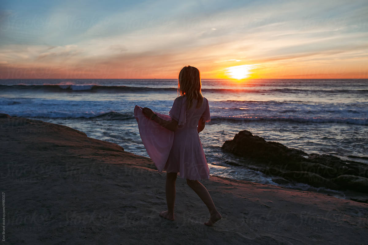 Happy tween girl with pink dress looking at a west coast sunset