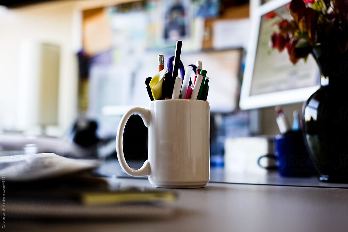 Mug full of writing instruments on a person\'s desk in an office