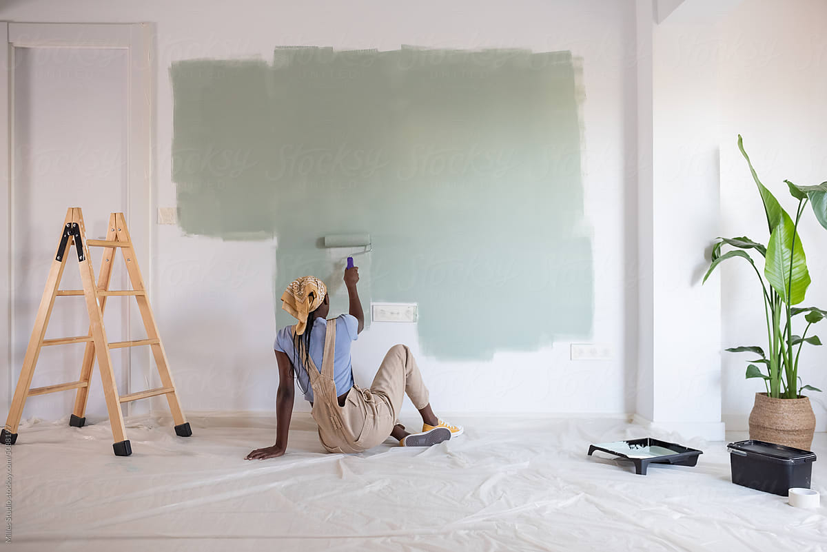 Black woman sitting on floor and painting wall