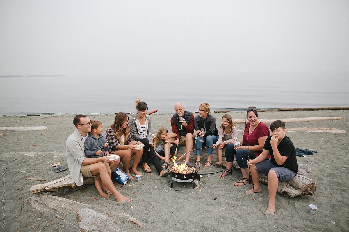 Multi generational family hanging out together around fire on the beach