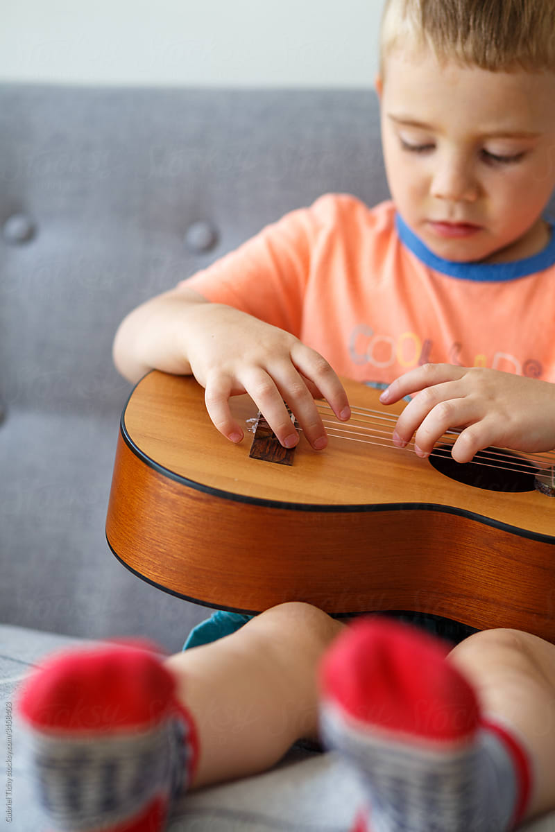Boy is exploring strings of a small guitar