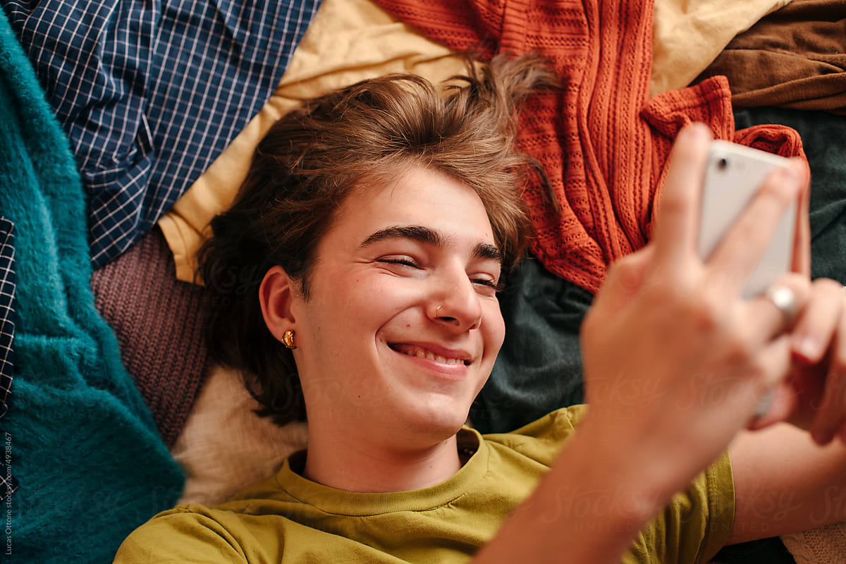 Smiling queer teen scrolling on his cellphone