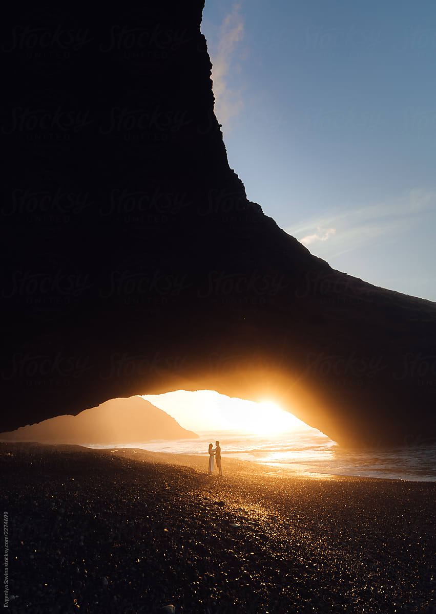 A couple deeply in love standing under the natural arch during the sunset enjoying the view