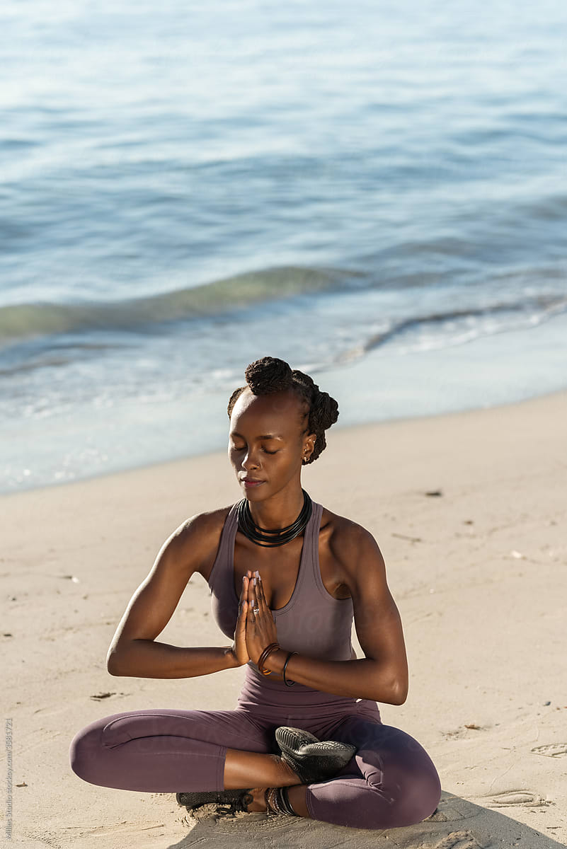 Black woman meditating in Lotus pose near sea